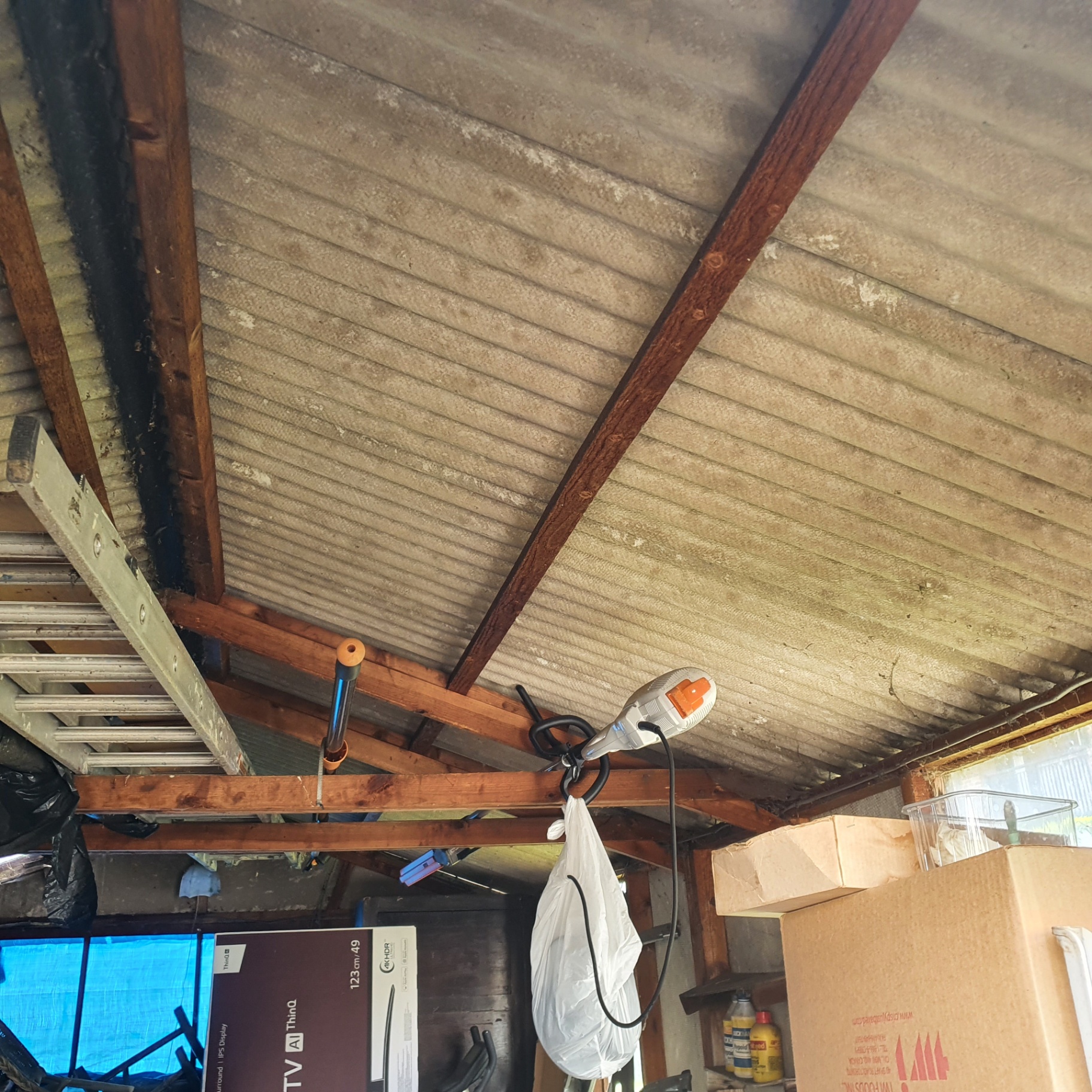 Underside of a corrugated asbestos cement garage roof showing fibrous surface and timber rafters.