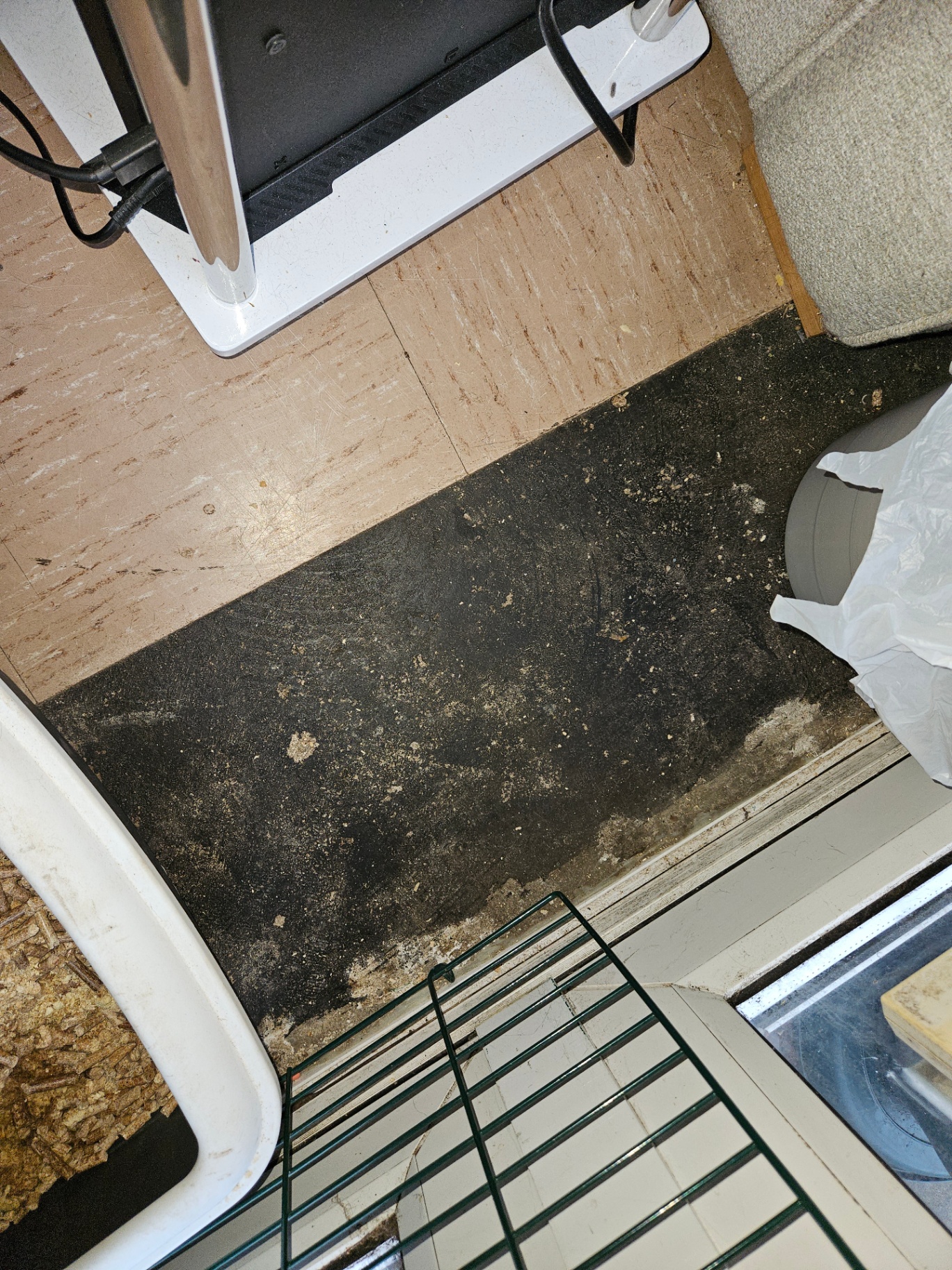 Beige thermoplastic floor tiles partly lifted to reveal a large area of black bitumen adhesive under a kitchen appliance.