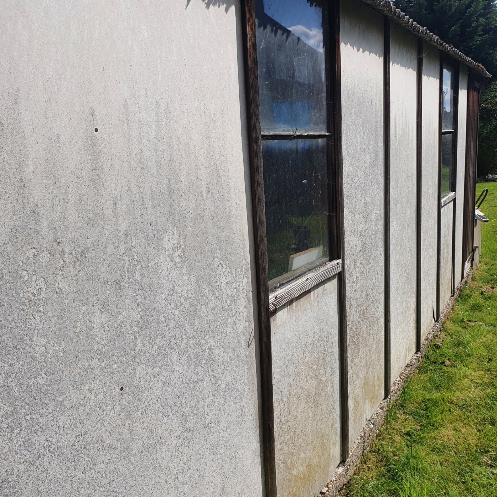 External asbestos cement wall panels on a prefabricated outbuilding showing surface weathering.