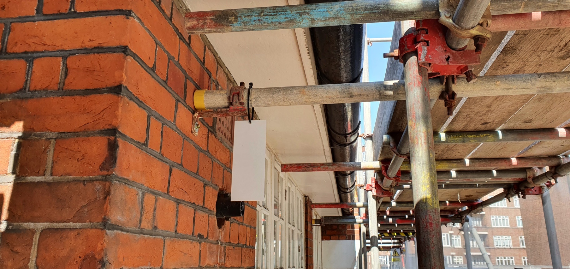Asbestos cement soffit board behind scaffolding on a commercial brick façade in London.