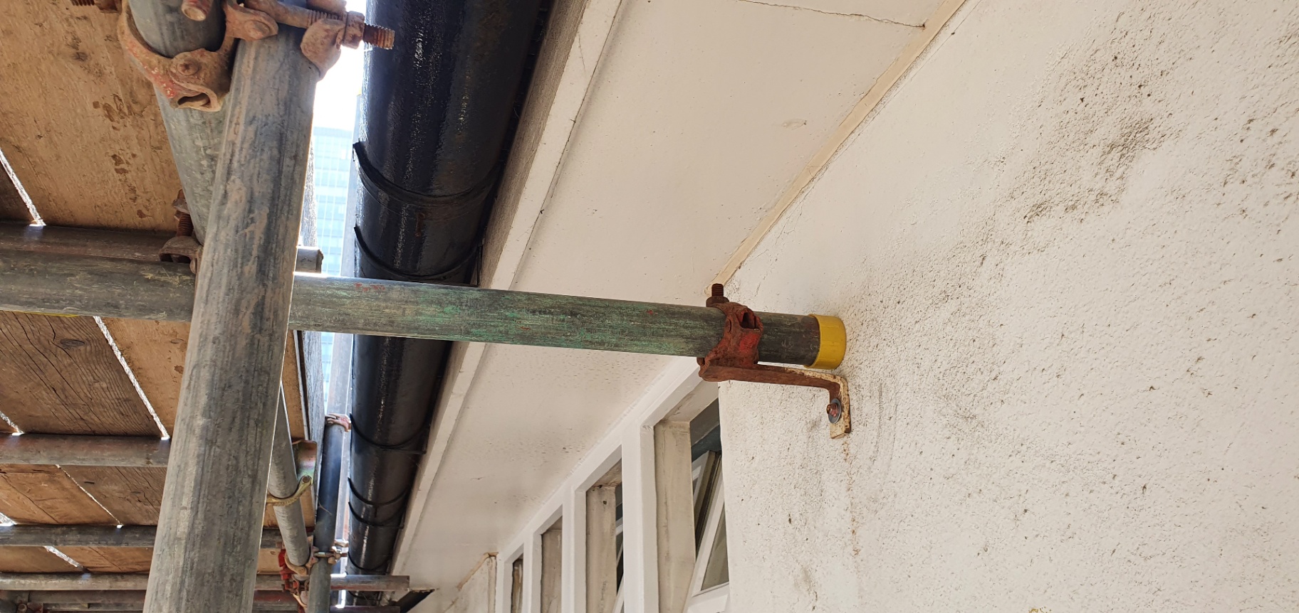 Close-up of a painted asbestos cement soffit board inspected from scaffolding.