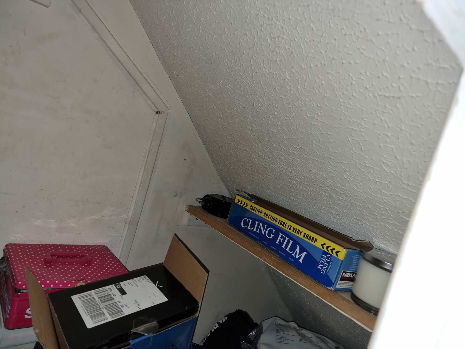 Textured coating applied to a sloping cupboard ceiling beside a panelled wall in a domestic storage area.