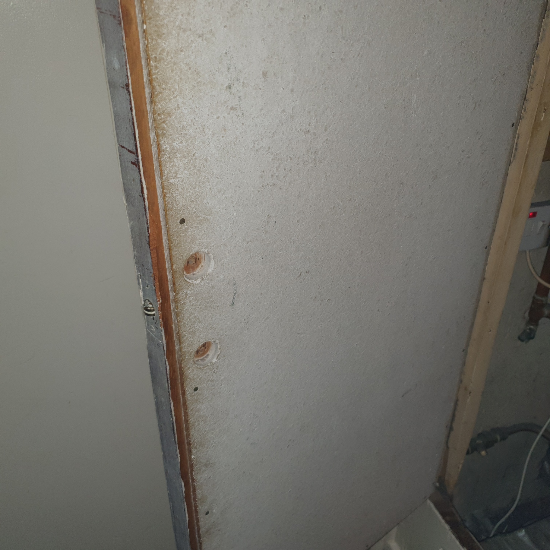 Asbestos insulating board lining inside an airing cupboard with drilled holes exposing the matrix.