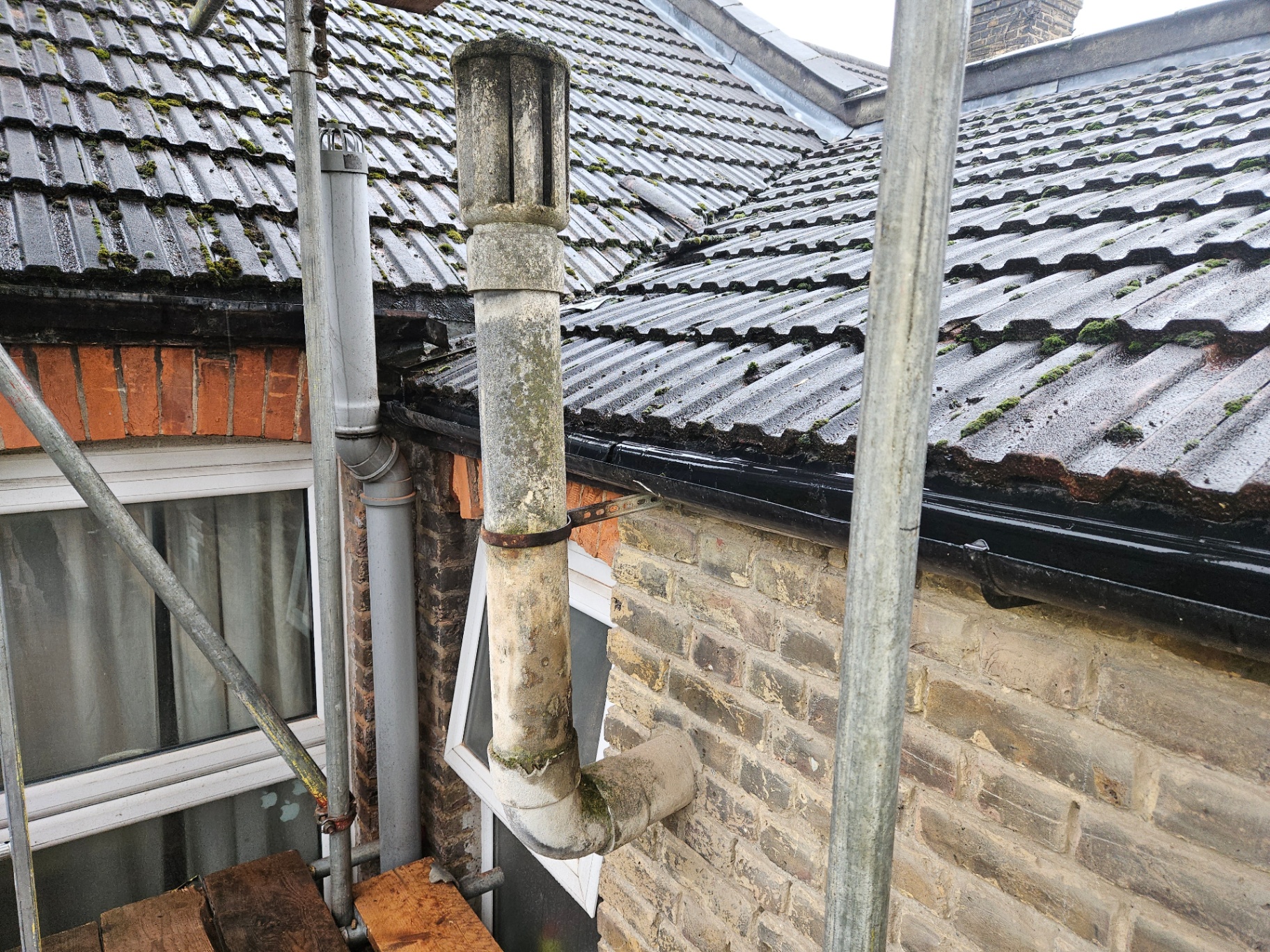 Weathered asbestos cement soil and vent pipe with terminal running up the rear elevation of a brick terraced house.