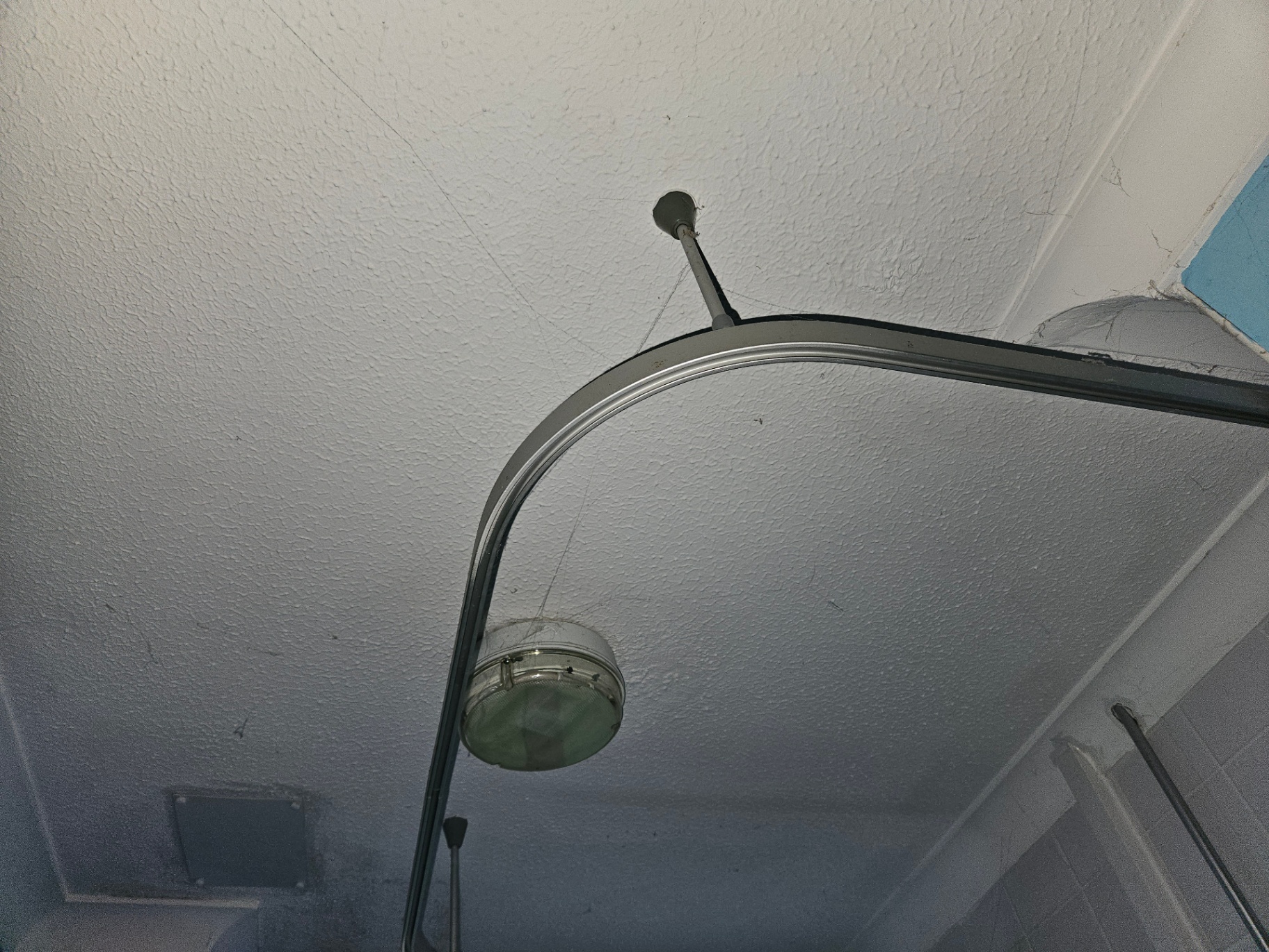 Stipple-finish textured bathroom ceiling with shower curtain rail and ceiling-mounted light fitting.