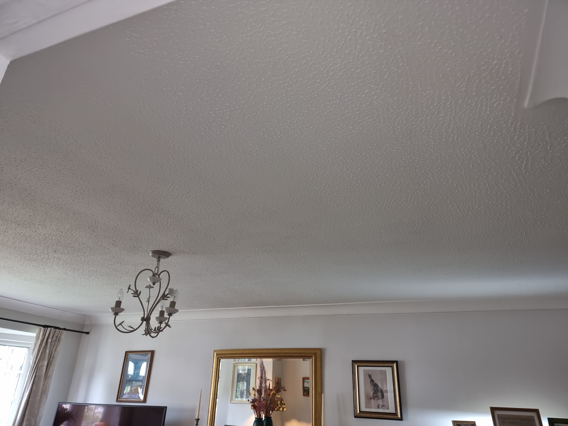Wide living room ceiling finished with textured coating above a chandelier and framed wall art.