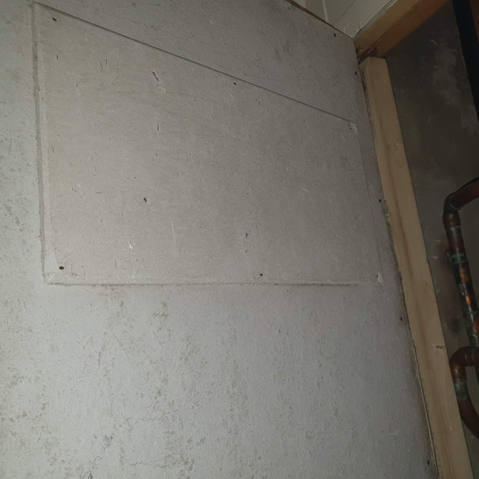 Asbestos insulating board access panel to a service riser in a domestic boiler cupboard.